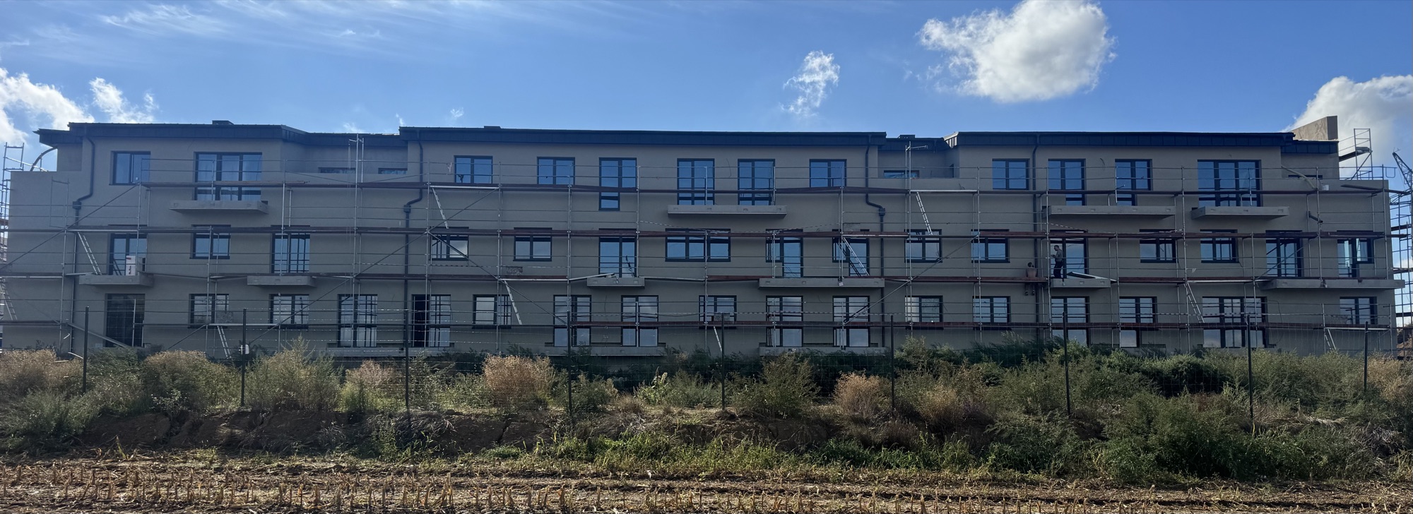 Průběh výstavby — detail fasády s lešením, práce na balkonech